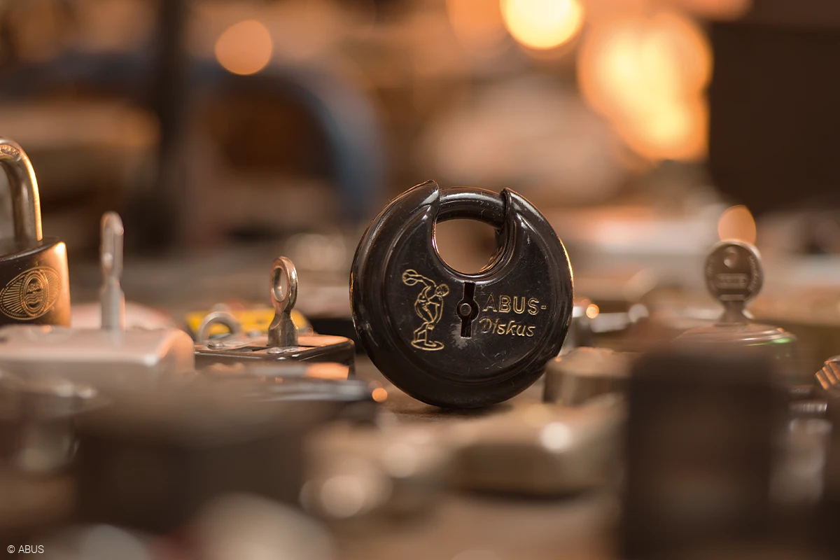 An unrecognisable surface on which various blurred padlocks lie, in the centre of which is a black Diskus lock in focus © ABUS